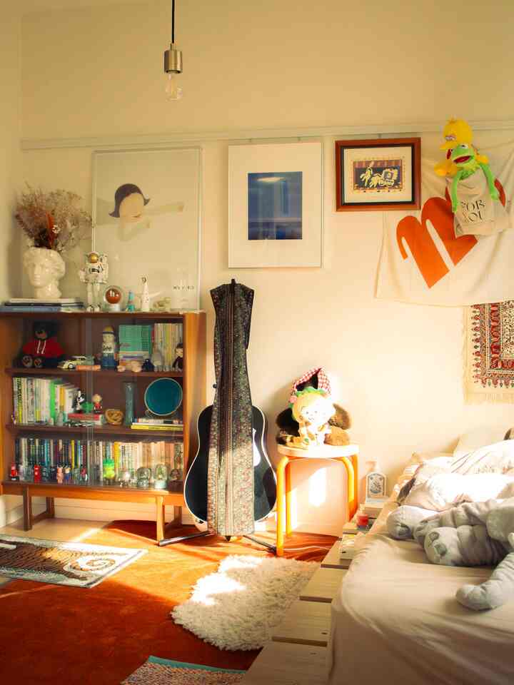 白と茶色のトーンが調和した1LDKのリビング兼寝室、ヴィンテージ家具とオレンジのラグが温かみのある雰囲気を演出する空間