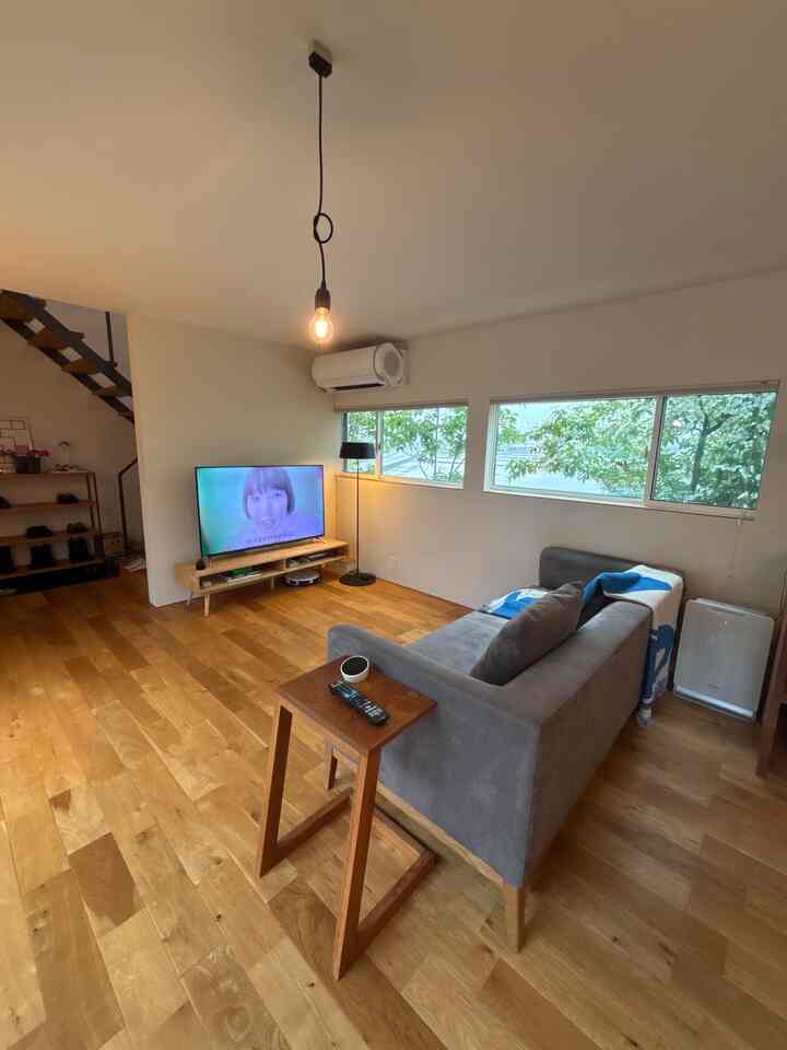 ナチュラルな木製床とグレーのソファが配置された北欧風リビング、テーブルなしで広々とした印象的な空間