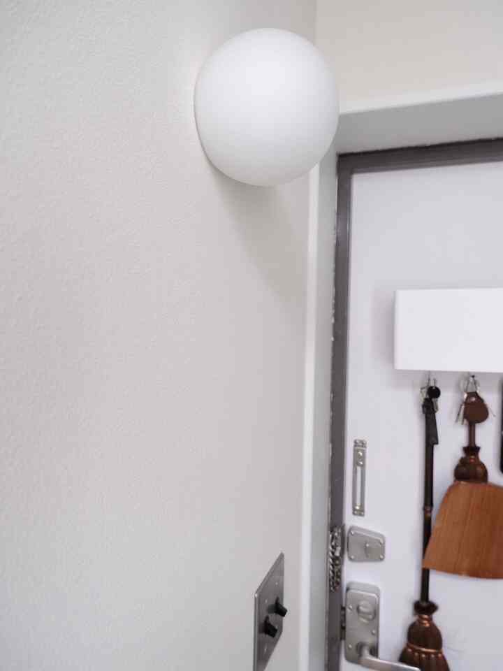 白を基調とした狭い玄関、壁付け照明があり、ドアに様々な玄関小物が掛けられている雰囲気のあるインテリア