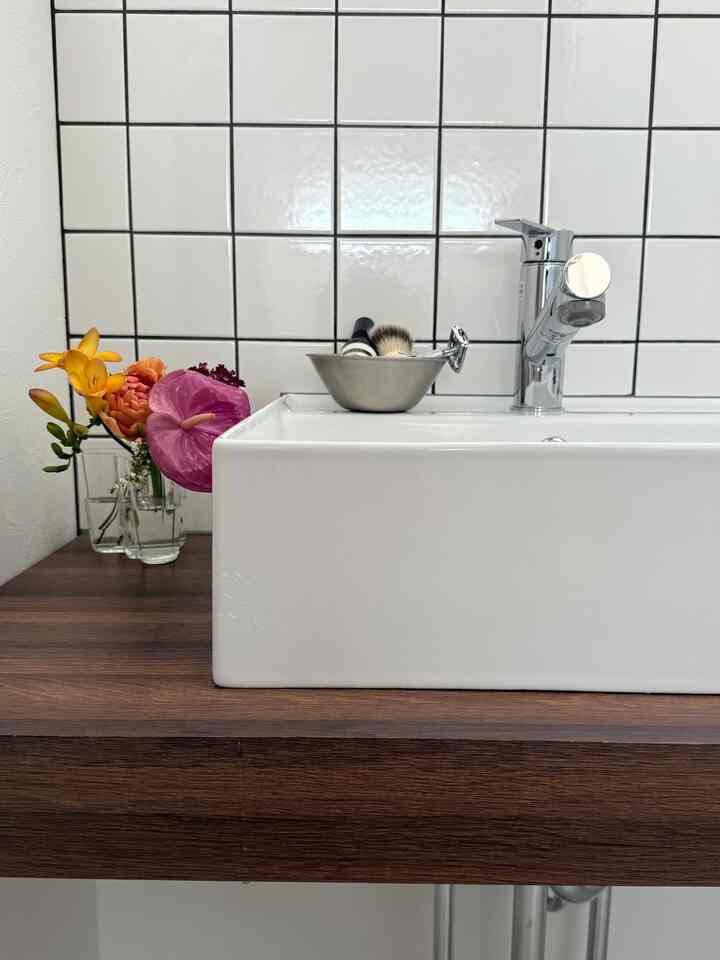 白と木目調が調和したバスルームの洗面台、花瓶とシェービングブラシが置かれたすっきりとしたミニマルなインテリア