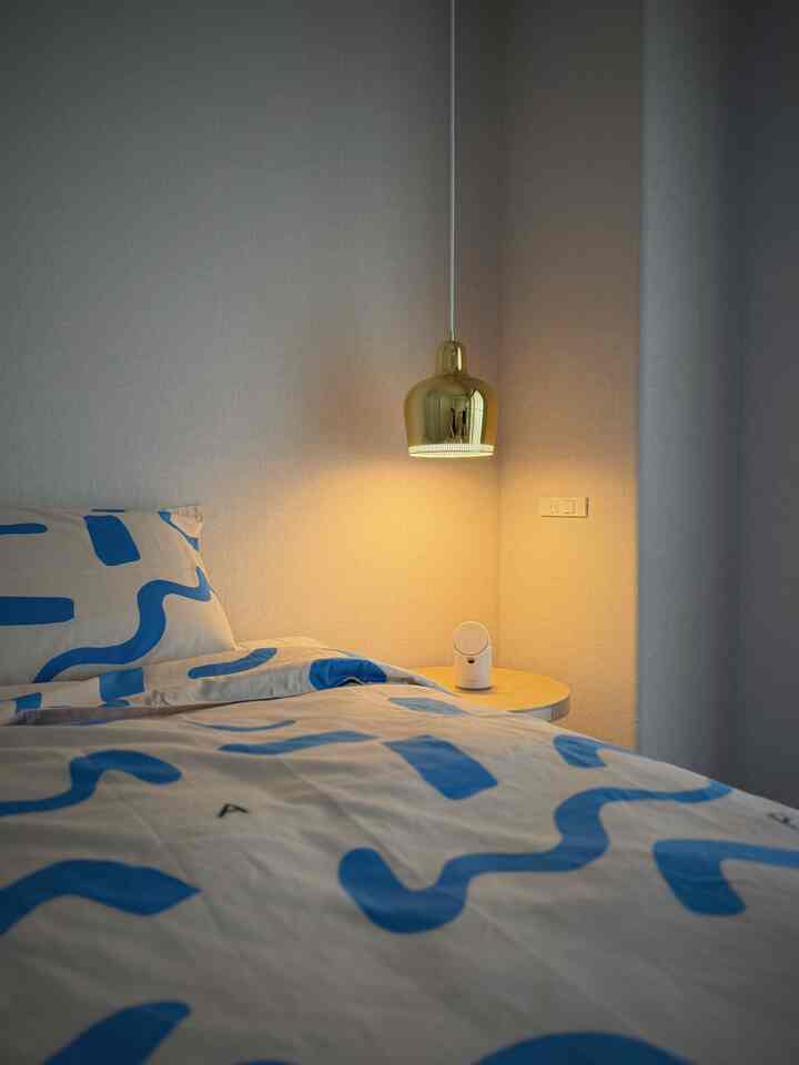柔らかなナチュラルトーンの寝室、ゴールドのペンダントライトと青の柄付き掛け布団カバーが配置された居心地の良い空間