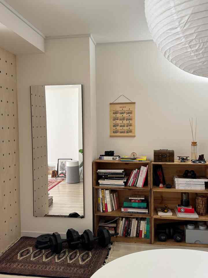 ナチュラルな色調の小さな部屋、木製の本棚と大きな鏡が配置されたミッドセンチュリーモダンの印象的な空間