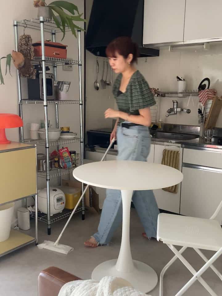 White-tone studio living and kitchen space featuring a round dining table and metal shelving in mid-century modern style
