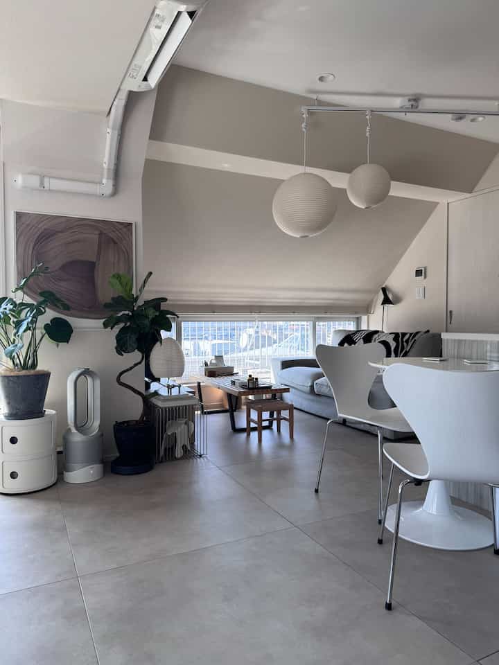 白とナチュラルな色調のリビングルーム、北欧スタイルのダイニングチェアとソファ、植物とペンダントライトが調和した雰囲気のあるインテリア