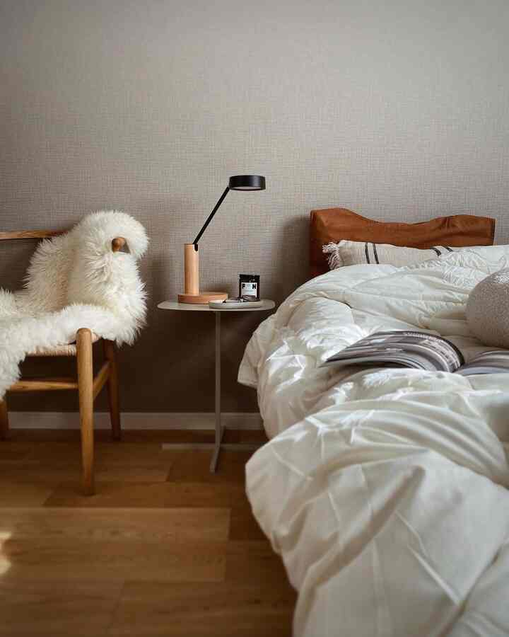 ホワイトとブラウンの色調の寝室、木製のアームチェアとテーブルランプが配置された、落ち着いた雰囲気のインテリア