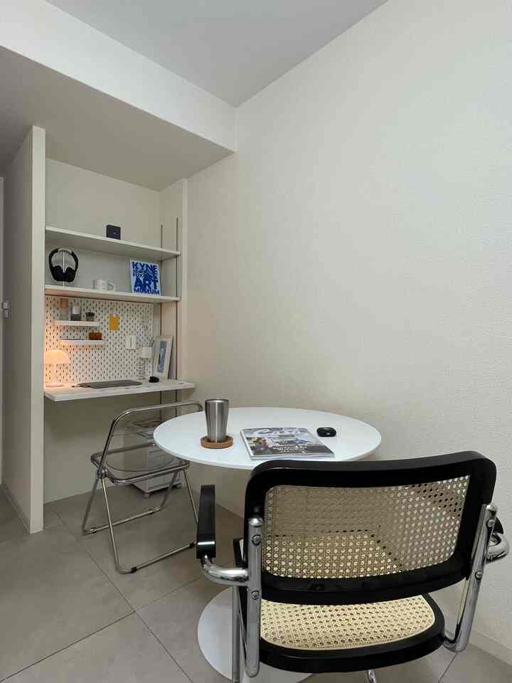 White walls and natural rattan chair in a compact 1K space featuring wall-mounted desk and round dining table, a neat home office and dining room combo