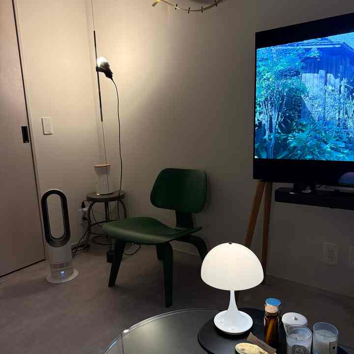 温かみのある白い壁とミッドセンチュリーモダンスタイルの緑色の椅子が配置されたコンパクトなリビングルーム