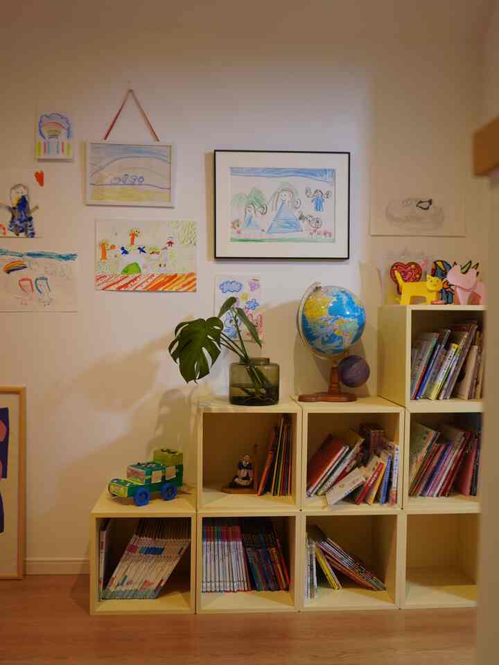 White-walled kids' room featuring beige bookshelves filled with books, toys, and children's drawings creating a cozy space