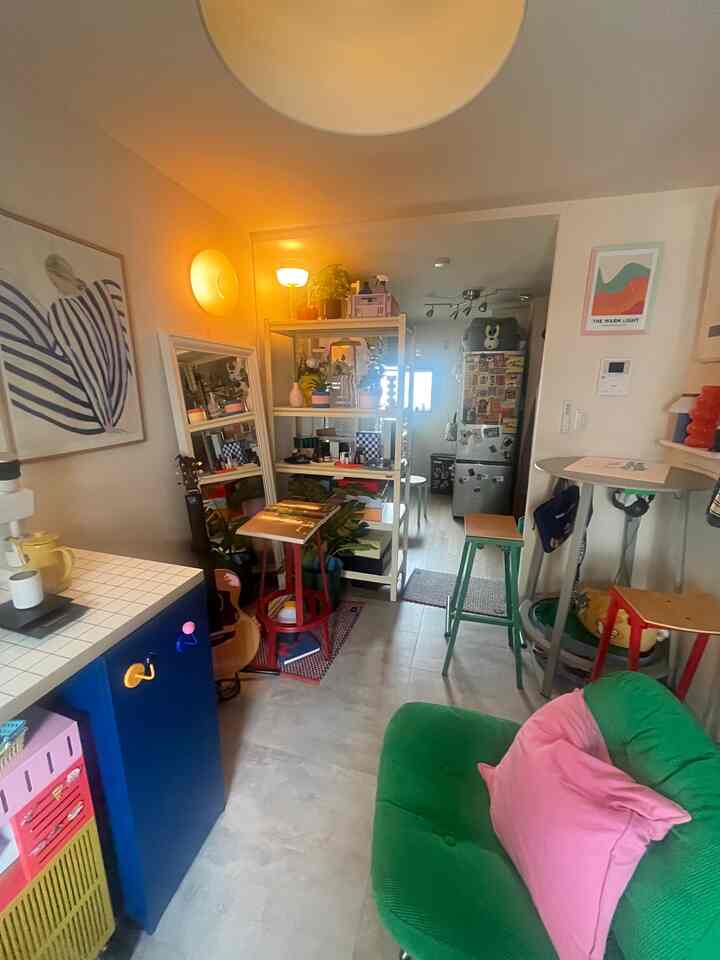 白い壁と緑のソファ、キッチンと棚が配置された居心地の良い一人暮らしのコンパクトな空間