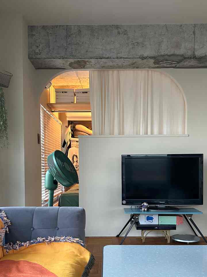 ブルーとイエローのトーンが特徴のワンルームリビング、ソファやテレビ、収納が配置されたモダンで居心地の良いインテリア