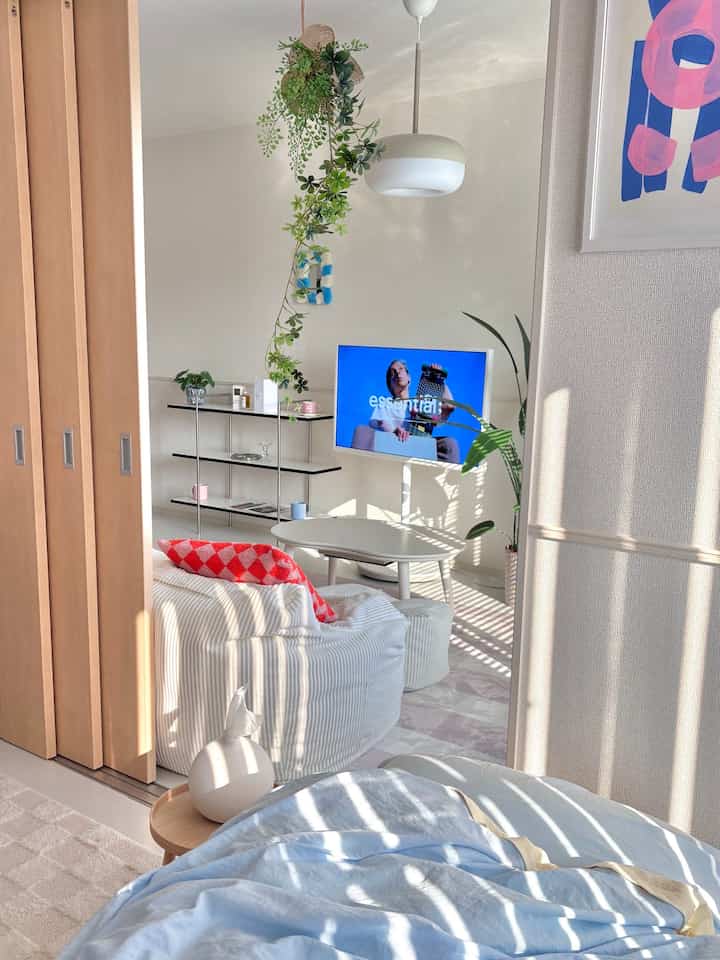 Bright natural-toned studio apartment living room featuring simple modern sofa, TV stand, and greenery creating a cozy atmosphere