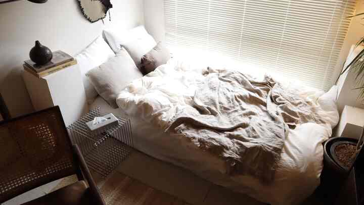 白とベージュ調の寝室、無印良品の掛け布団カバーと自然なブランケットが配置された雰囲気のあるインテリア