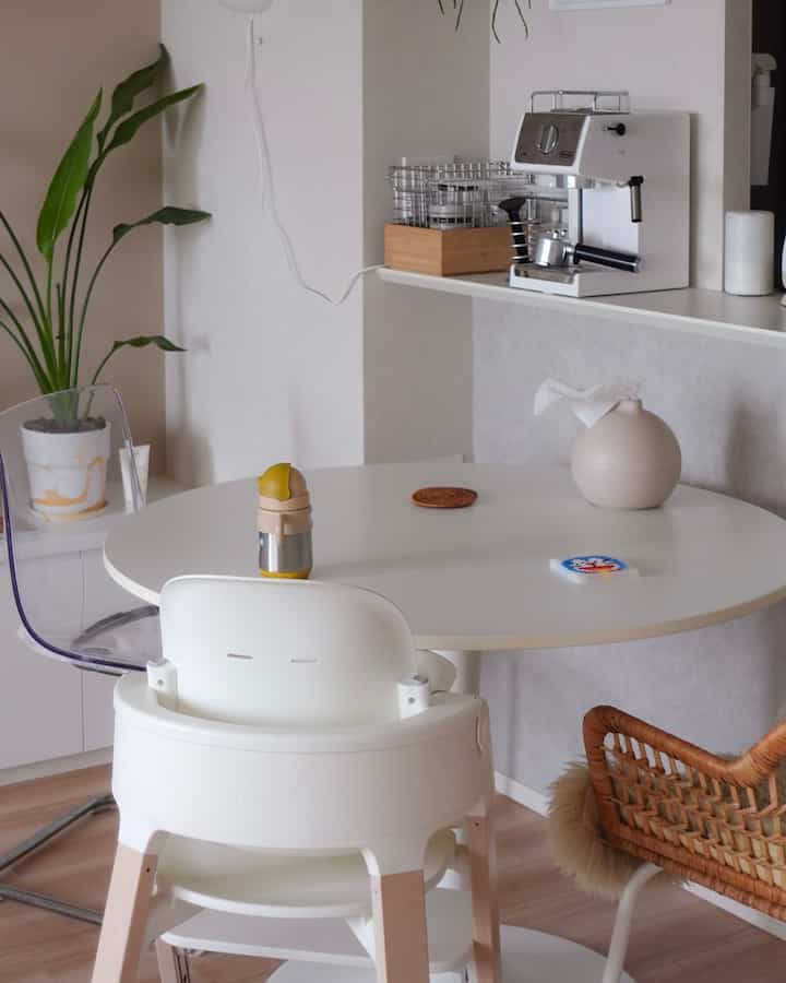 ホワイトとウッドトーンのリビングダイニング、子供用ハイチェアとコーヒーマシンが配置された雰囲気のある空間