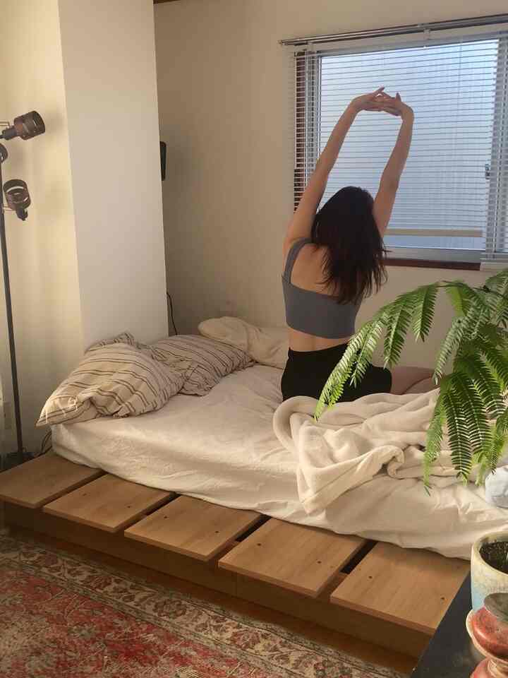 White-toned walls with wood tone bed frame and floor lamp in a natural modern bedroom space