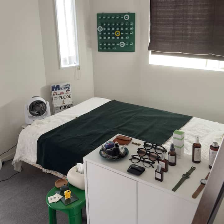 Cozy bedroom with white walls and dark green blanket, neatly arranged personal items and white storage cabinet in a small room