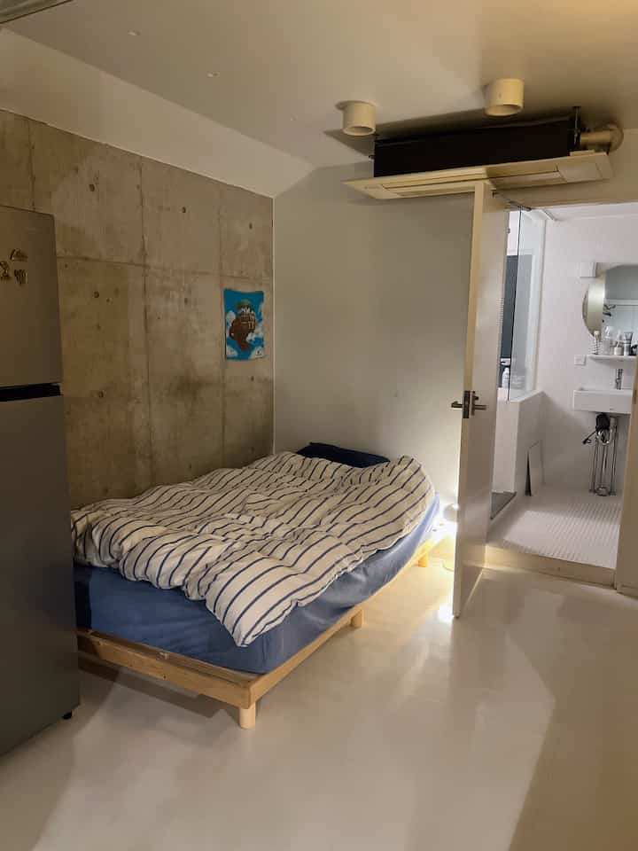Blue and natural toned small hotel-like bedroom featuring a minimalist striped duvet cover and an open bathroom door