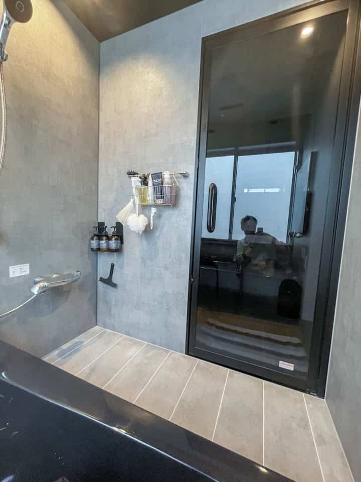 グレーの壁と床、黒い浴槽とガラス戸が配置されたモダンなバスルームの空間