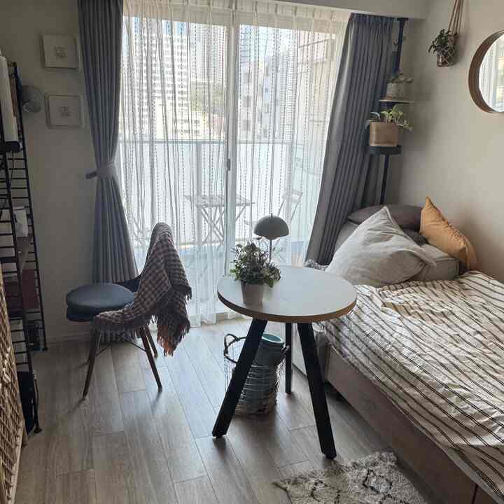 ナチュラルな色調のコンパクトなワンルーム、ベッドと丸テーブル、植物が配置された温かみのある空間