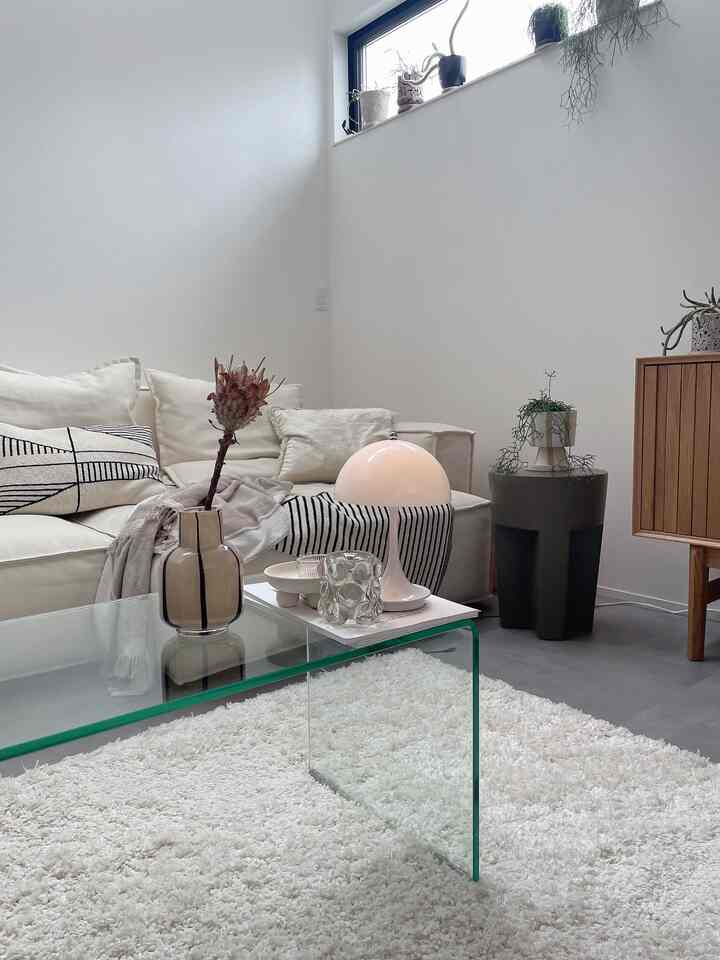 白とベージュのナチュラルカラーのリビング、モダンなソファと透明なガラステーブル、植物が配置された落ち着いたインテリア