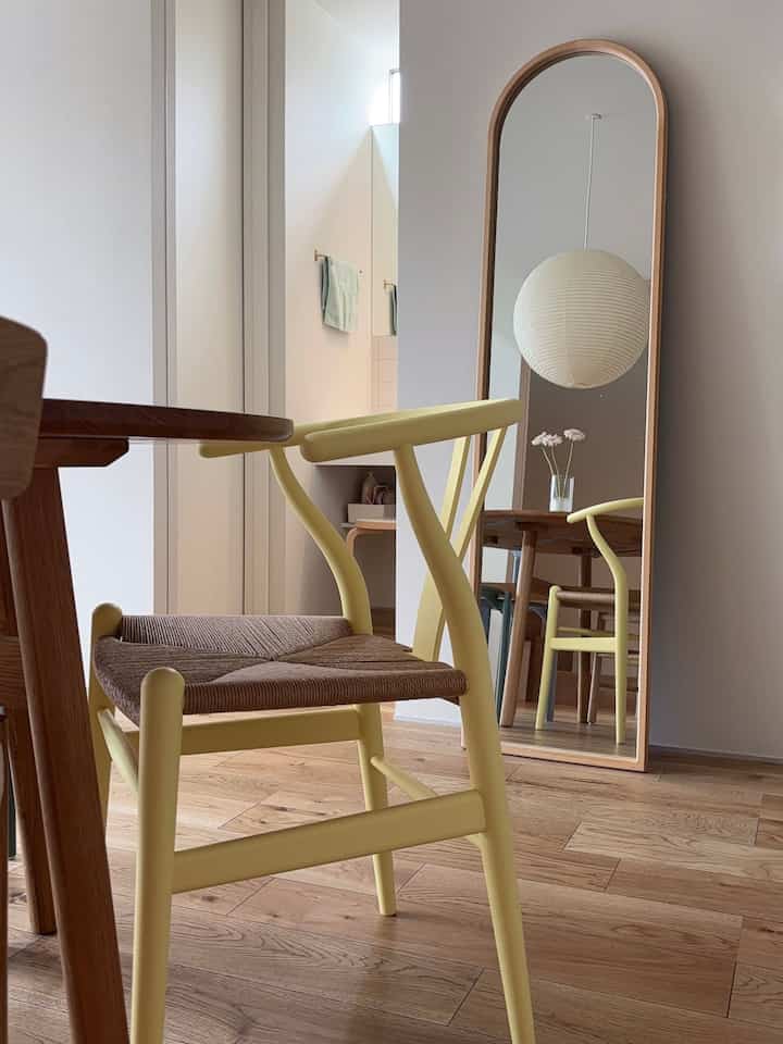 Natural modern dining room with white walls, wood-tone flooring, pale yellow dining chairs, an arched full-length mirror, and a round pendant light