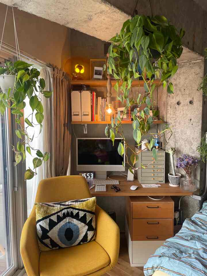 Natural tone home office with abundant green plants, cozy desk corner featuring yellow chair and wooden desk