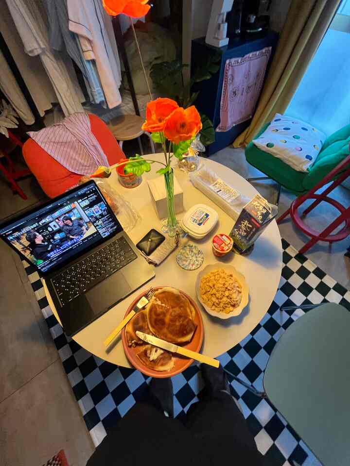 カラフルなカフェ風ダイニングルーム、中央の丸テーブルに朝食とノートパソコンが置かれた雰囲気のあるインテリア