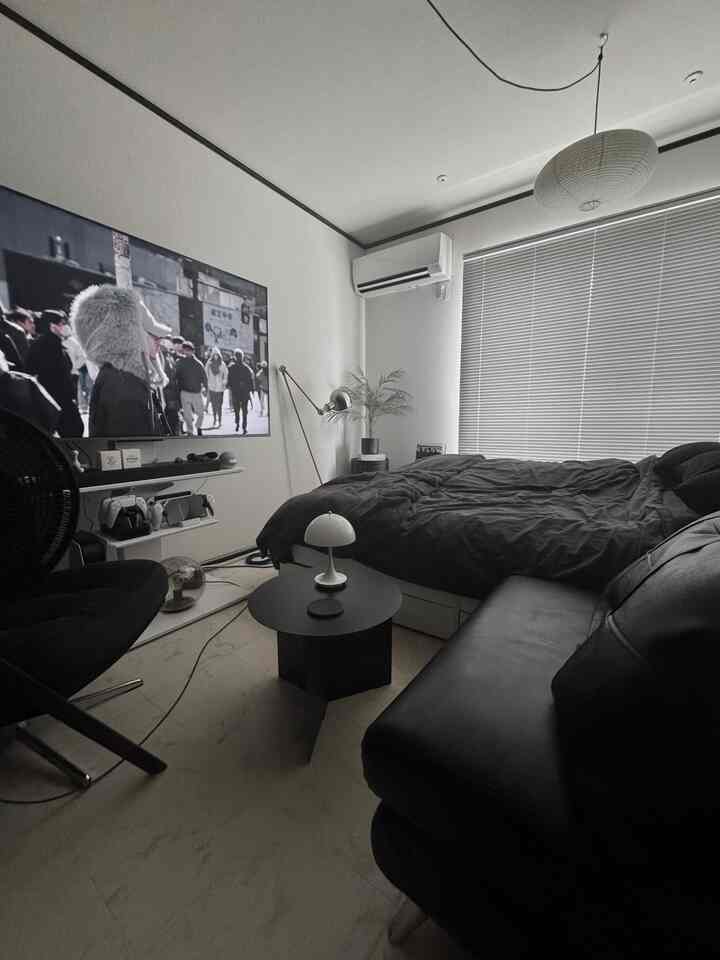 黒と白のトーンの寝室、モダンなベッドとソファ、大型テレビ、ペンダントライトが配置された落ち着いた空間