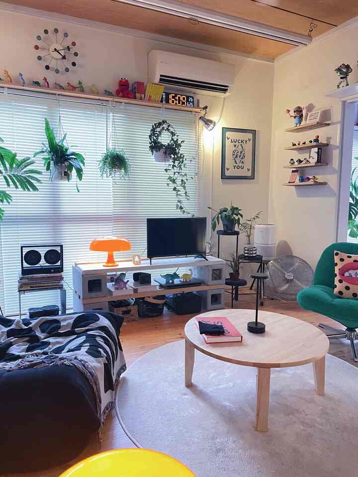 Bright natural-toned living room with round coffee table, green armchair, shelving and plants arranged on walls creating cozy atmosphere