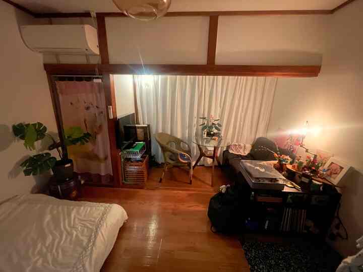 ナチュラルカラーの6畳間でリビング兼寝室、白いカーテンとソファ、植物が配置された雰囲気のあるインテリア