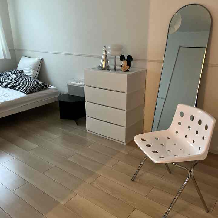 モノトーンの白い寝室、白いチェストと穴あきチェア、黒いサイドテーブルが配置されたシンプルなインテリア