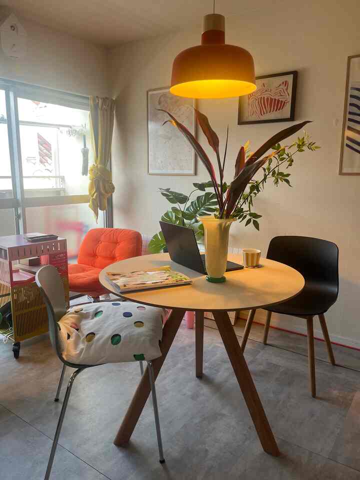 オレンジのペンダントライトと丸いダイニングテーブルがある1LDKのミッドセンチュリーモダンスタイルのダイニングルーム、様々な椅子と植物が配置された空間
