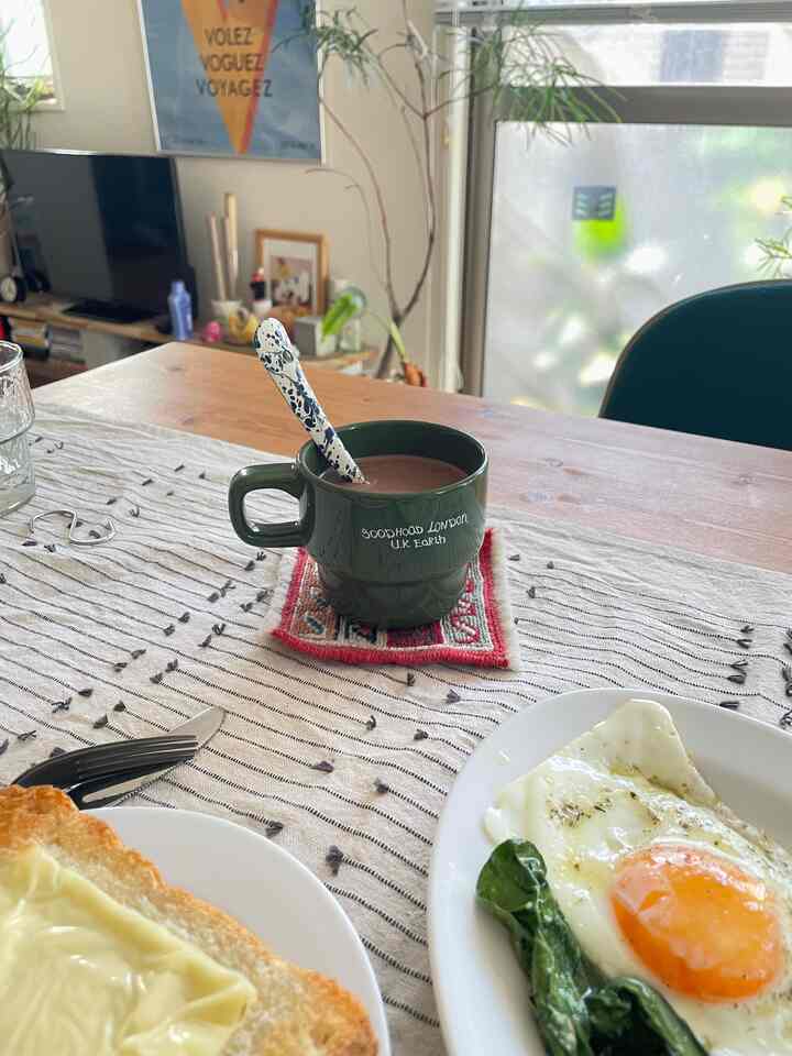 ウッドトーンとグリーンのアクセントがある1LDKのダイニングルーム、木製のダイニングテーブルとグリーンのマグカップが配置されたおうちカフェの雰囲気のあるインテリア