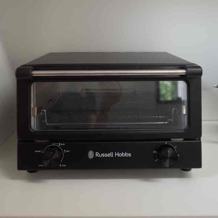 黒いRussell Hobbsのオーブントースターが白い壁と棚の上に置かれたシンプルなキッチンスペース