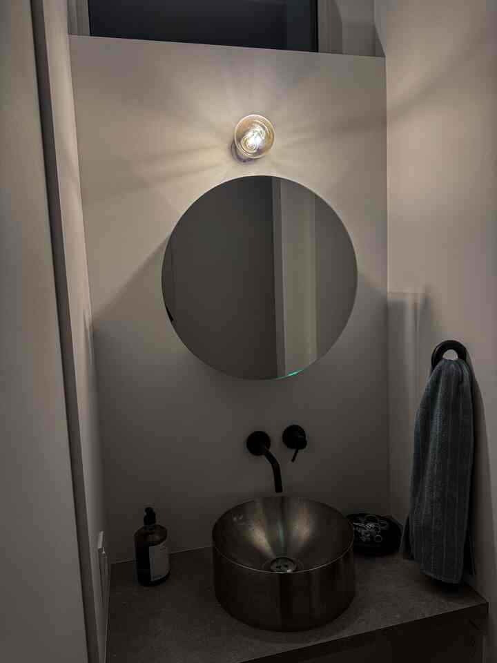 ナチュラルカラーのモダンな狭いバスルーム、丸い鏡と黒い蛇口、青いタオルが配置された清潔感のある空間