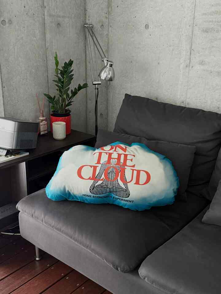 グレーのソファと雲形クッション、コンクリート壁とフロアランプが配置されたモダンな一人暮らしのリビング