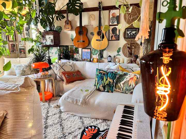 白とナチュラル色調のリビング、居心地の良いソファと植物、ボヘミアンスタイルのウォールアートが配置された雰囲気のある空間