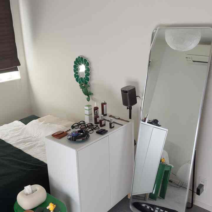 白を基調とした小さな寝室、中央の白いキャビネットと左の緑色の寝具が調和するミニマルな空間