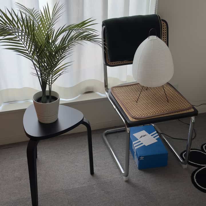 ナチュラルなカフェ風の室内、黒いスツールとラタンチェアに独特な照明が配置された落ち着いた空間