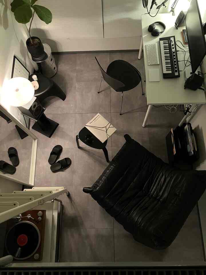 ブラックとグレーのトーンでまとめられたコンパクトなホームオフィス空間、黒いレザーソファとデスク、ミニシンセサイザーが配置されたミニマルなインテリア