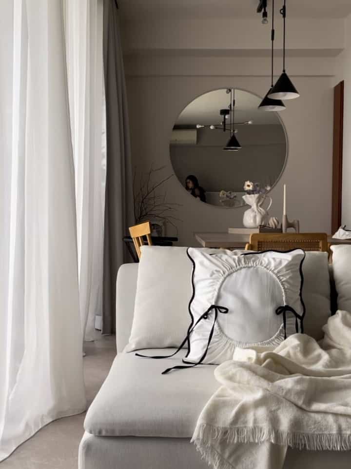 Bright white-toned living and dining room featuring large round mirror and pendant lights in a modern interior