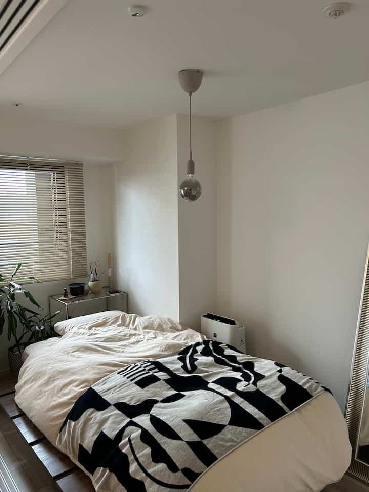 ホワイトとベージュの色調の寝室、ナチュラルモダンなベッドと鏡、植物が配置された落ち着いた雰囲気のあるインテリア