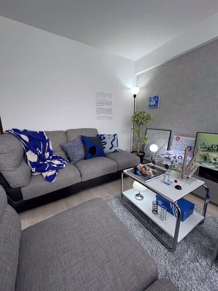 グレーとブルーのトーンのリビング、広いグレーのソファとブルークッション、フロアランプがある清潔でモダンな空間