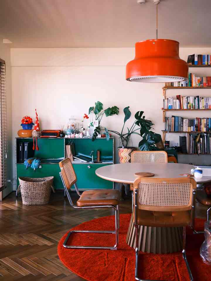 鮮やかな赤いペンダントライトとラグが際立つ、ヴィンテージ調の緑色キャビネットとダイニングテーブルが配置されたナチュラルカラーのダイニングルーム