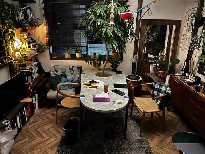 ブラウンの木目調とグレーの色合いが調和したリビング、中央に植物のあるダイニングテーブルと北欧スタイルの椅子が配された落ち着いた空間