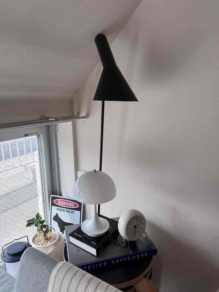 ホワイトとブラックが調和するリビングのコーナー、フロアランプとテーブルランプがスツールの上に置かれ、時計と本が並ぶナチュラルモダンな印象的な空間