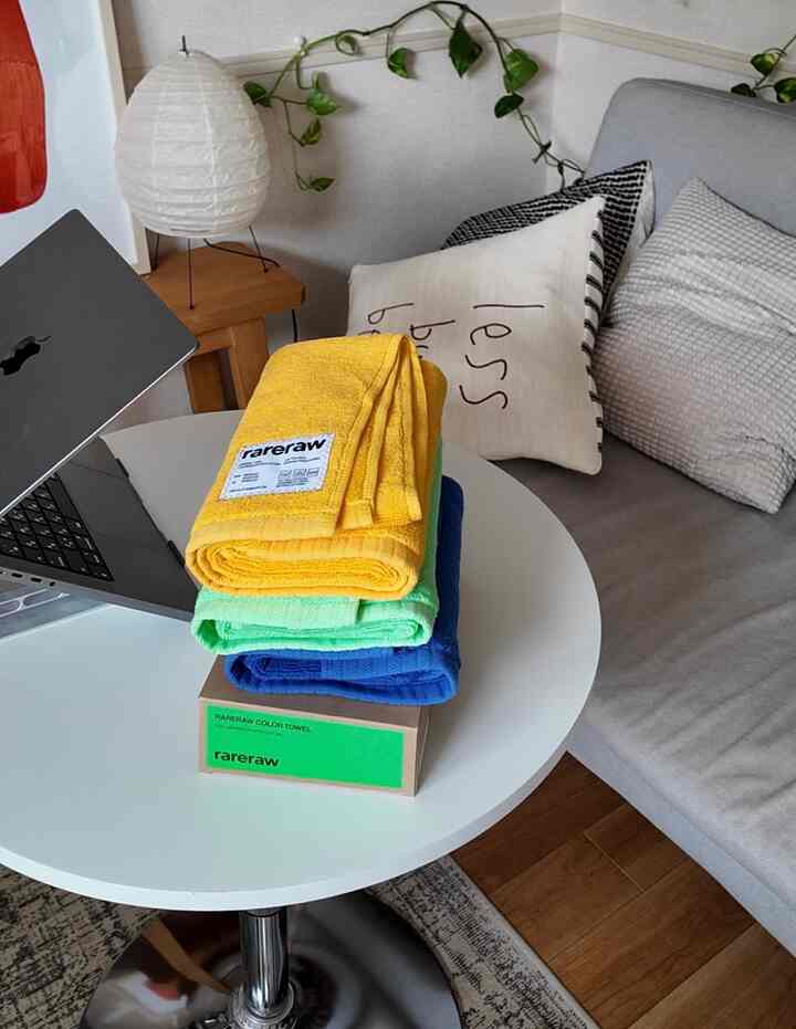 ホワイトとベージュの色調のリビングルーム、ホワイトの円形テーブルにカラフルなタオルとノートパソコンが置かれた雰囲気のあるホームオフィス空間