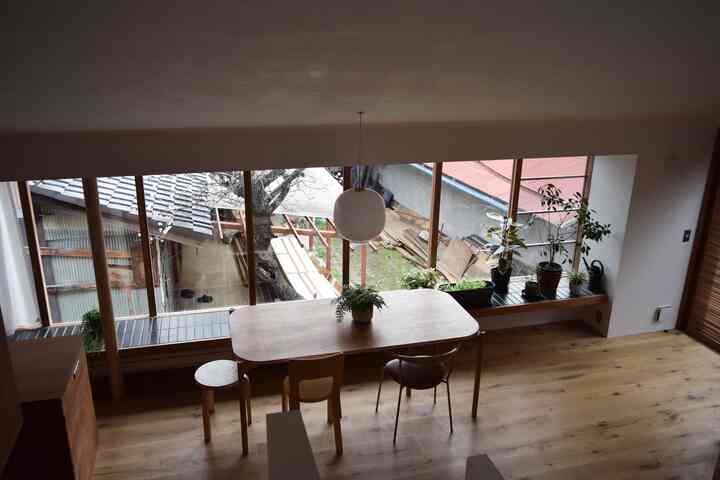 Natural wood tone dining room with large windows, featuring a simple dining table and chairs in a cozy atmosphere
