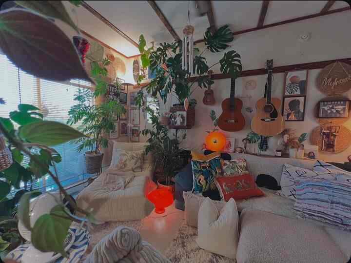 ナチュラルな色調のリビングルーム、多様な植物とくつろげるソファ、壁掛けギターとウォールアートが調和した雰囲気のある空間