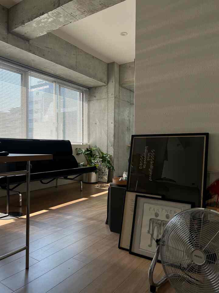 Charcoal and wood tone living room featuring blinds, black sofa, and a silver floor fan creating a comfortable atmosphere