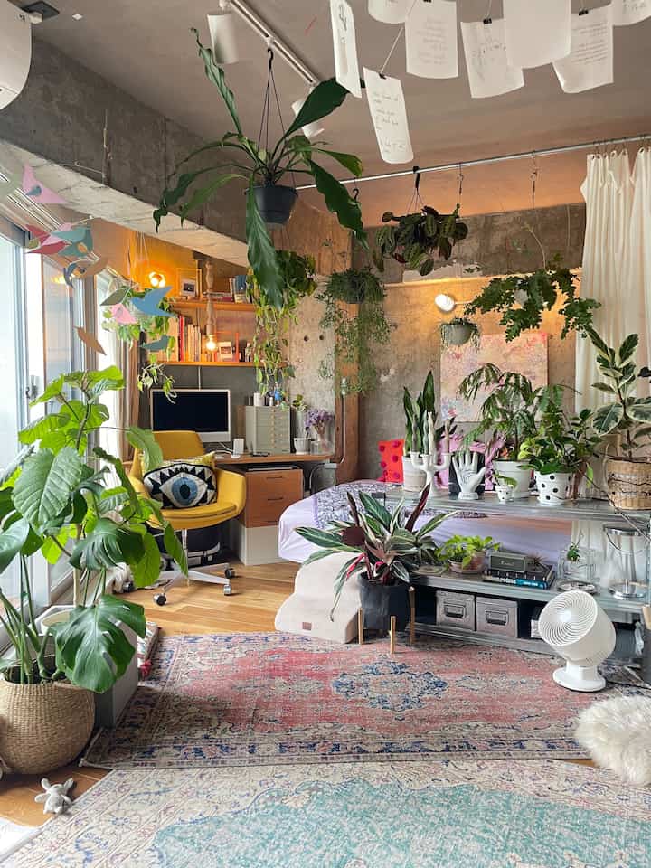 ナチュラルトーンの寝室、ヴィンテージスタイルのデスクと本棚が配置され、多数の植物が調和した雰囲気のあるインテリア